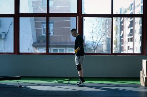 Young man exercising with a skipping rope in an urban gym with large windows and city view.
