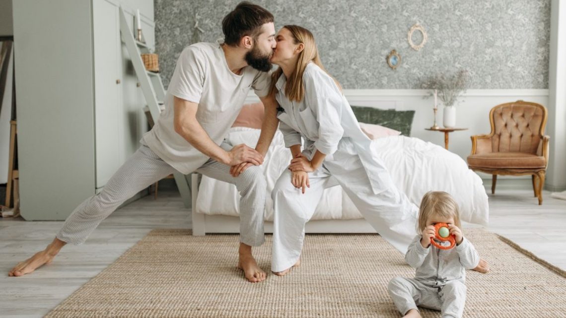 Playful morning with parents stretching and a toddler playing in the bedroom.