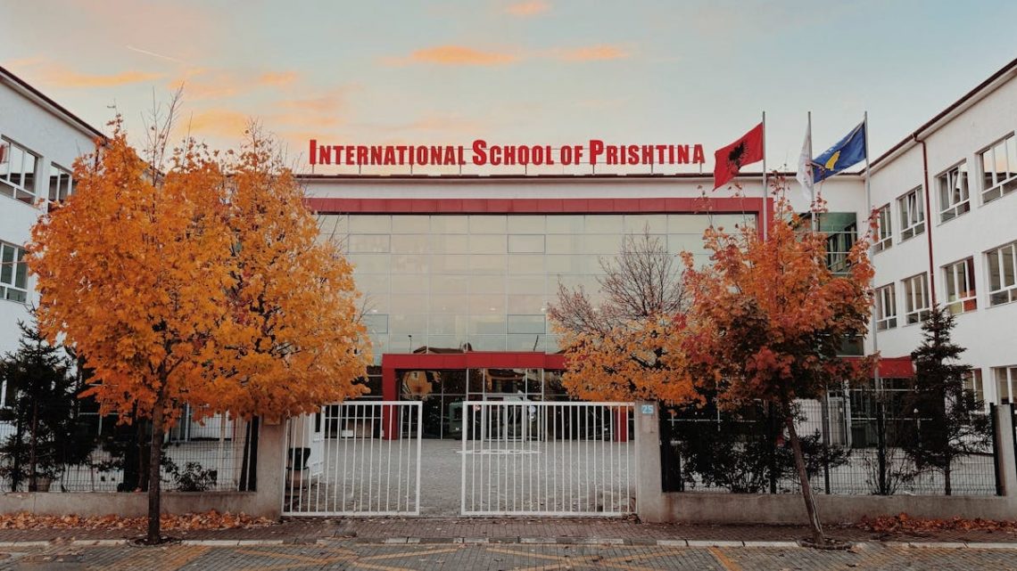 Front view of International School of Prishtina with autumn trees and flags.