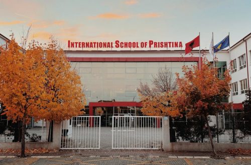 Front view of International School of Prishtina with autumn trees and flags.